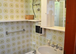 Uma casa de banho com azulejos estampados, uma pia, um espelho, uma prateleira com uma cesta e um aquecedor.