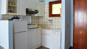A compact kitchen with white cabinets, a stove, a sink, and a window. - House Agave (Moneglia)