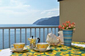 A table with two yellow cups and a coffee pot, a potted plant, and a seashell on a balcony overlooking the sea. - House Agave (Moneglia)
