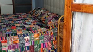 A room with a bed covered in a colorful patchwork quilt, a wooden headboard, and a sliding glass door. - House Agave (Moneglia)