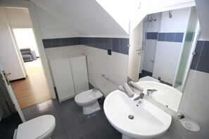 A modern bathroom with a toilet, bidet, and sink. There is a shower area visible in the background. - House Ducale (Genoa)