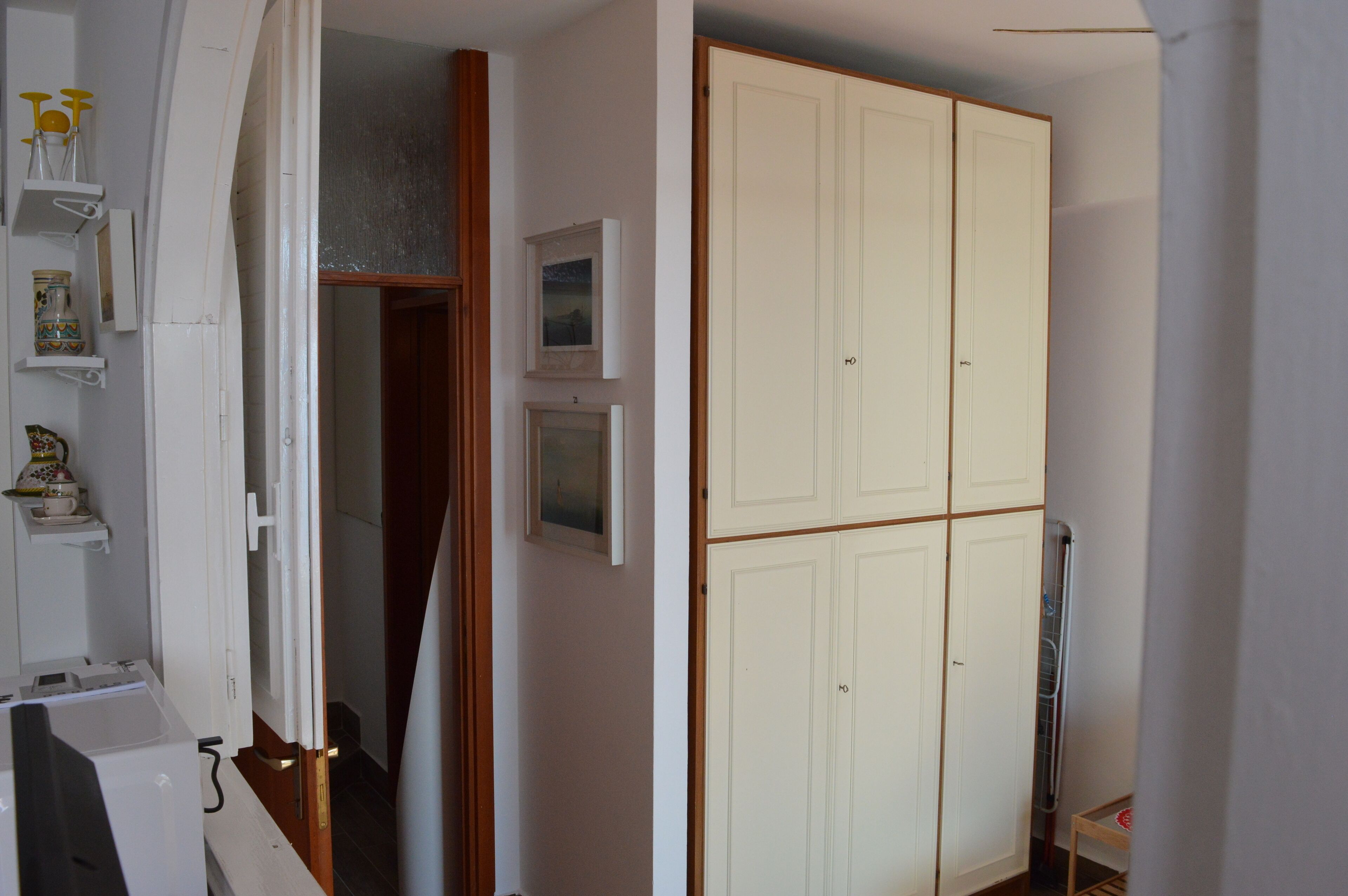 A room with a wardrobe, a small table, and a shelf with decorative items.