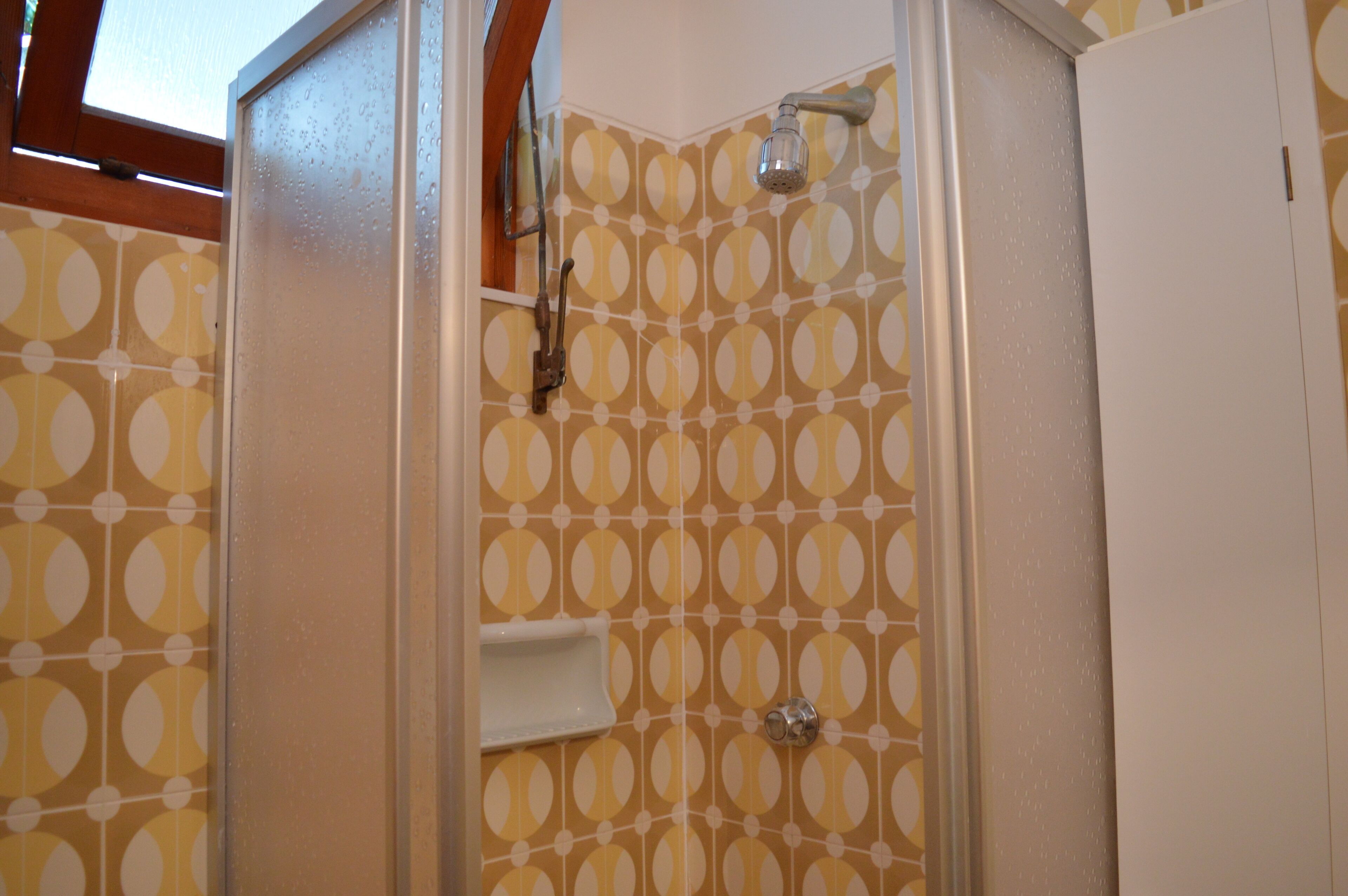Een douche met een wand betegeld in een cirkelvormig patroon, een witte deur en een zichtbare douchekop.