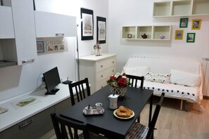 A compact living space with a dining table, chairs, a sofa, a small kitchenette, and a few decorative items. - House Bia (Genoa)