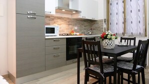 A modern kitchen with grey cabinetry, a microwave, an oven, and a dining area with a table and chairs. - House Bia (Genoa)