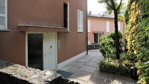 Un bâtiment doté d’une porte, d’une fenêtre et d’un petit jardin avec des plantes et un arbre.