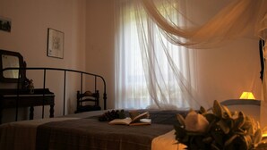 Une chambre à coucher avec un lit, une table de chevet, une lampe et une fenêtre avec des rideaux légers.