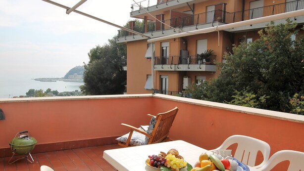 Un balcon avec une table dressée pour un repas, un barbecue vert et une vue sur la mer.