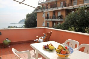 A balcony with a table set for a meal, a green grill, and a view of the sea. - La Terrazza sul Golfo (Arenzano)