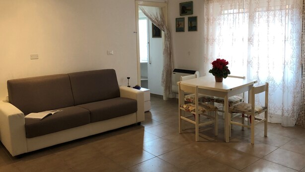 A living room with a sofa, a dining table with chairs, a potted plant, and a window with curtains. - House Orsa Maggiore (Bordighera)