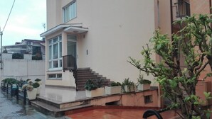 A modern building with a staircase leading to a balcony, surrounded by potted plants and a small garden area. - House Orsa Maggiore (Bordighera)