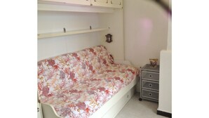 A small room with a white sofa bed with a floral cover, a small dresser with drawers, and a rug on the floor. - House Roberta (Recco)