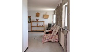 A living room with a sofa, a television, a console table with decorative items, and a stone wall. - House Roberta (Recco)