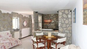 A dining area with a stone wall, a round wooden table, and white chairs. - House Roberta (Recco)