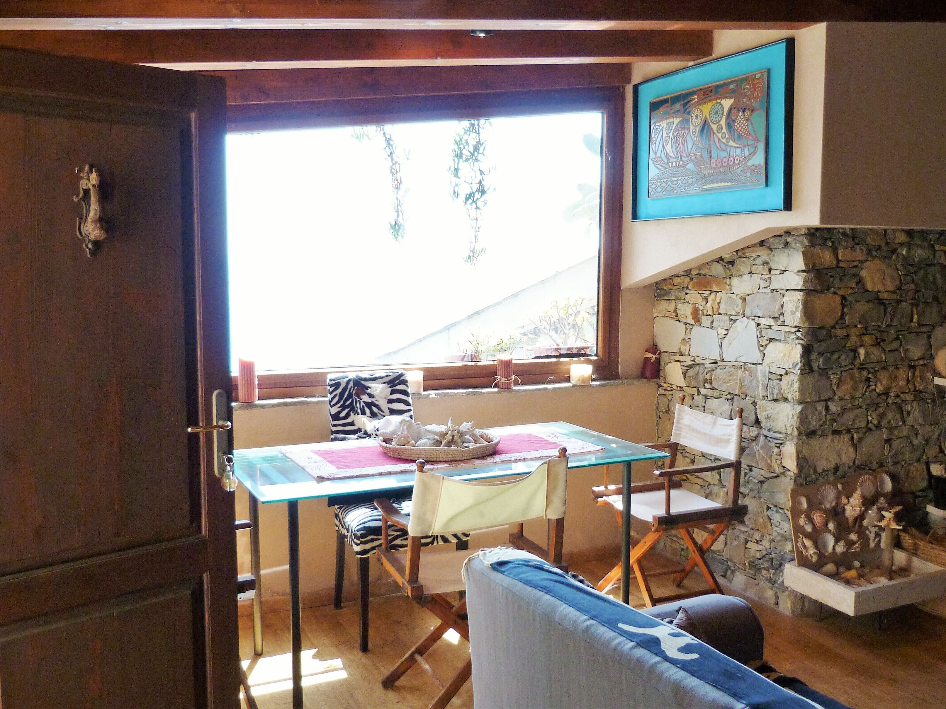 A cozy dining area with a table set for two, a stone fireplace, and a view of greenery outside.