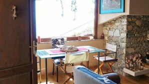 A cozy dining area with a table set for two, a stone fireplace, and a view of greenery outside. - House Limone (Recco)