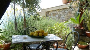 A table with a bowl of lemons, surrounded by potted plants and a stone wall. - House Limone (Recco)