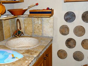 A kitchen with a stone sink, a wooden shelf with a bowl and a book, and a wall with circular plates. - House Limone (Recco)