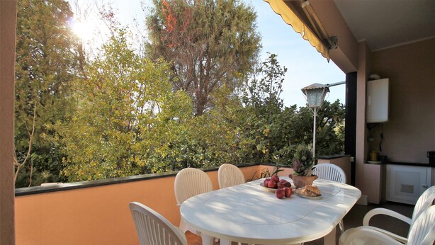 A round table with white chairs on an outdoor patio with a view of trees and a lamp post. - Il Quadrifoglio in Pineta (Arenzano)
