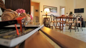 A dining area with a wooden table, chairs, and a lamp. There is a painting on the wall and a television mounted above the table. - Il Quadrifoglio in Pineta (Arenzano)