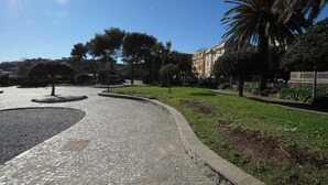 A paved pathway in a park with trees and a building in the background. - Il Quadrifoglio in Pineta (Arenzano)