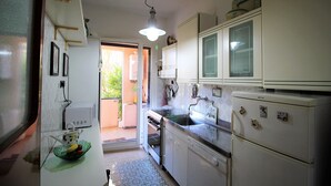 A compact kitchen with white cabinets, a sink, and a refrigerator. There is a window providing natural light and a door leading to an outdoor area. - Il Quadrifoglio in Pineta (Arenzano)