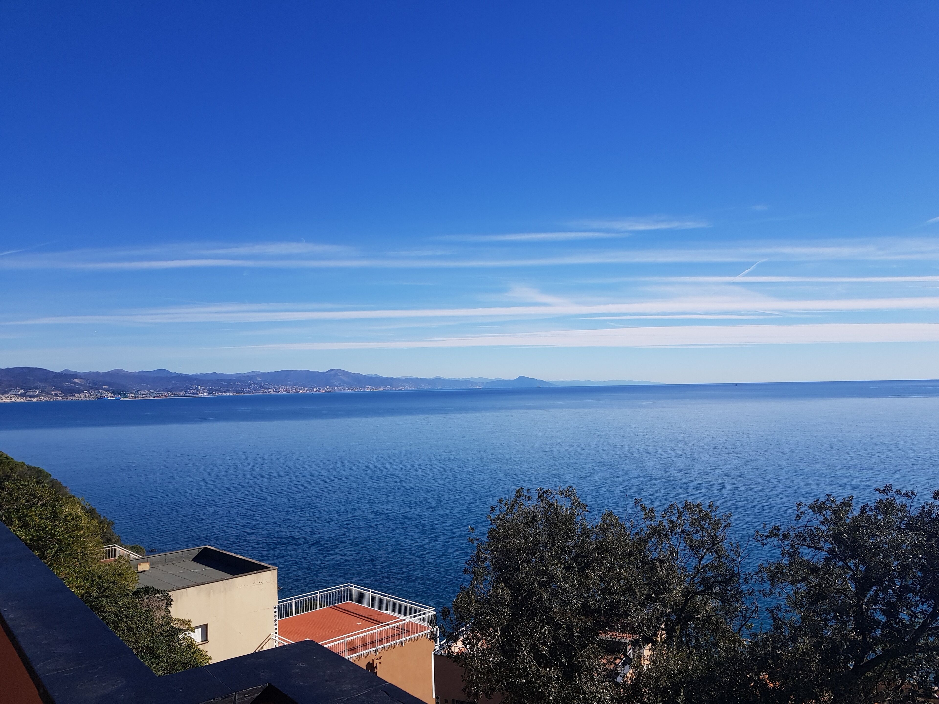 Une vue sur la côte, avec un ciel bleu dégagé, une mer calme et des montagnes à l’horizon.
