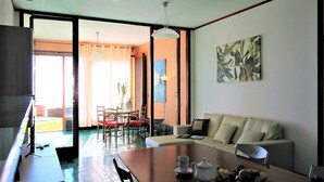 A modern living room with a dining table, sofa, and chairs. There is a large window providing natural light, and a painting on the wall. - Villa Limoni (Arenzano)