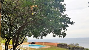 A pool with a view of the sea, surrounded by trees and a stone wall. - Villa Limoni (Arenzano)