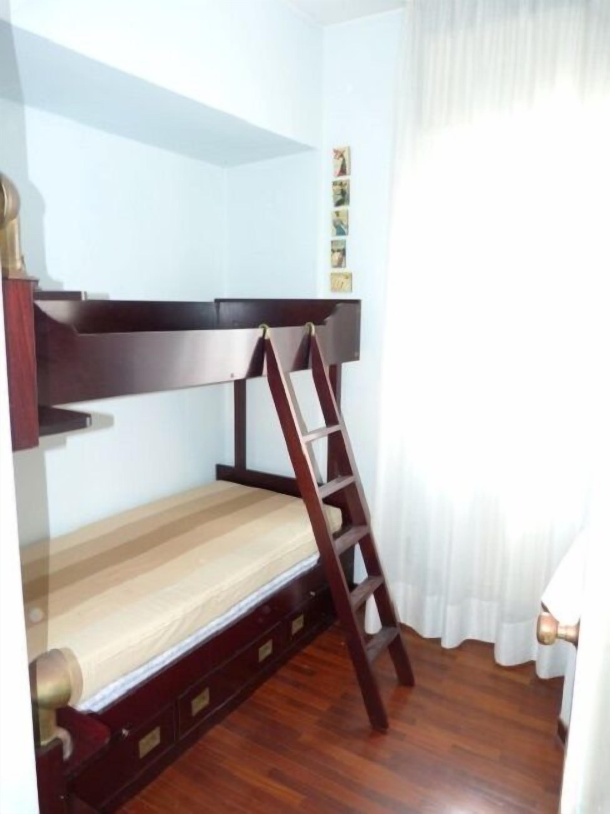 A bunk bed with a wooden ladder, a wooden desk, and a small cabinet.