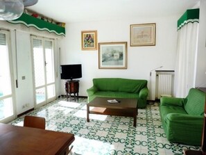 Un salón con un sofá verde, una mesa de centro y un televisor sobre un mueble. Hay dos cuadros en la pared.