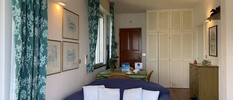 A bedroom with a bed, a bedside table with a lamp, a window with curtains, a door, and a hallway leading to a bathroom.