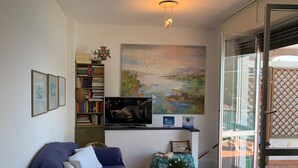 Uma sala de estar com sofá, televisão, estante de livros e um quadro.