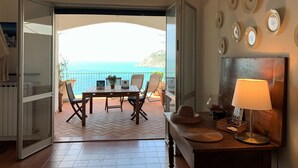 An open balcony with a table and chairs, a view of the sea, and a wall with decorative plates. - House Mediterraneo (Moneglia)