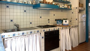 A kitchen with white tiles, blue shelves, and various kitchenware. - House Mediterraneo (Moneglia)
