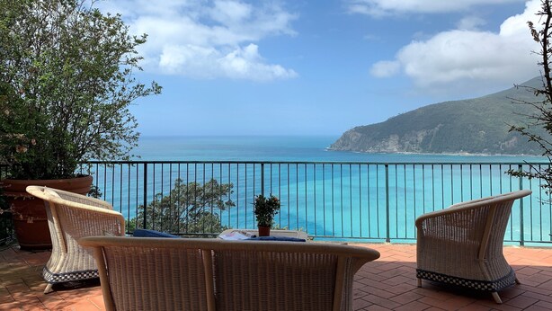 A balcony with wicker chairs and a table, overlooking a turquoise sea and a mountainous landscape. - House Mediterraneo (Moneglia)