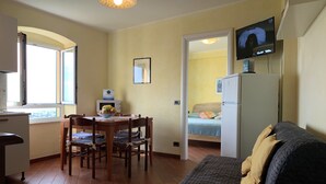 A compact living space with a dining area, a bed, a television, and a kitchenette. - House Blue Sky (Genoa)