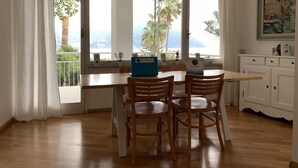 A dining area with a table and chairs, a laptop, and a view of the sea through large windows. - Villa Adele (Sori)