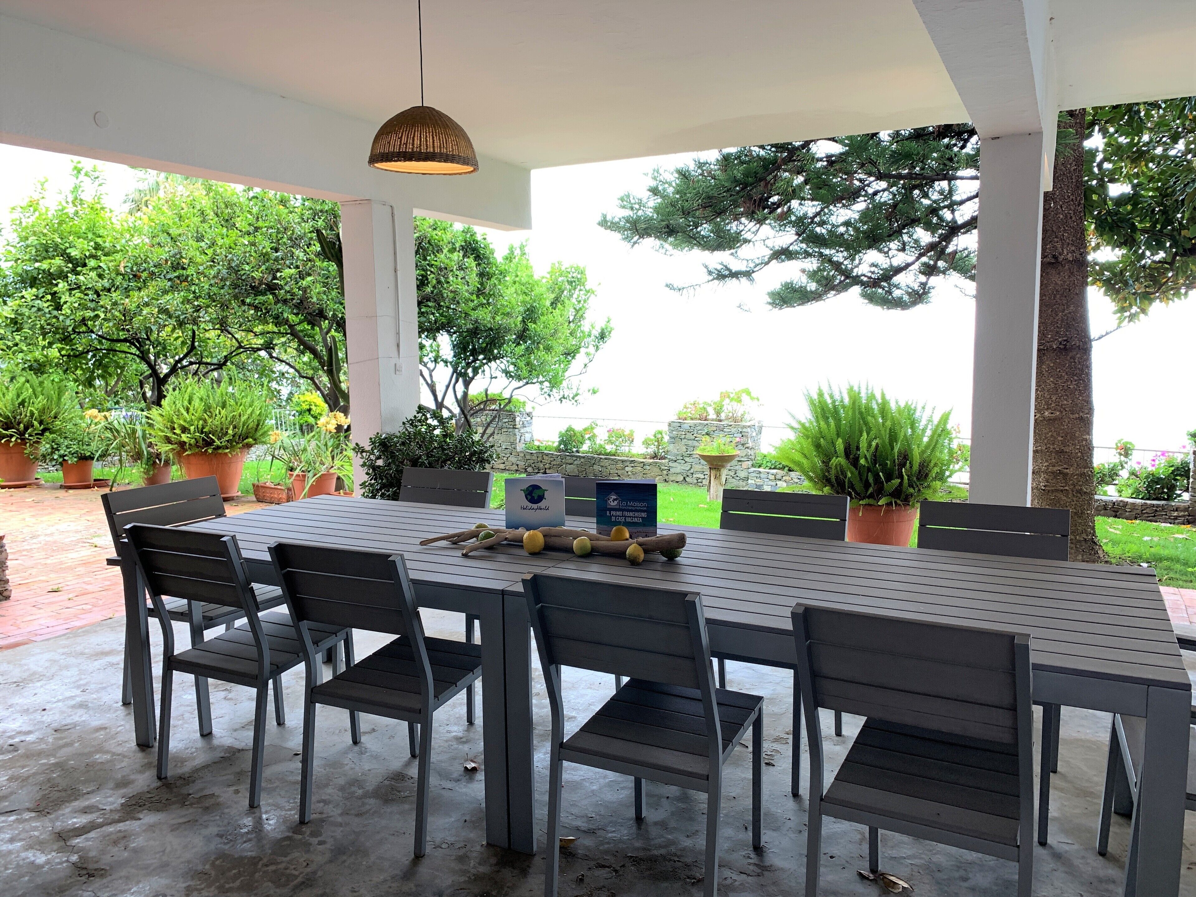 An outdoor patio with a table and chairs, surrounded by potted plants and trees.