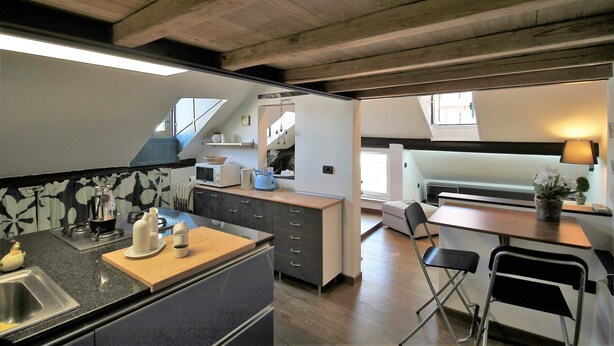 A compact kitchen with a central island, a dining area with a table and chairs, and a visible staircase leading to an upper level. - ILA1505 House Golia (Genoa)