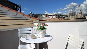 A rooftop terrace with a round table and two white chairs, a potted plant with pink flowers, and a view of the cityscape in the background. - ILA1505 House Golia (Genoa)