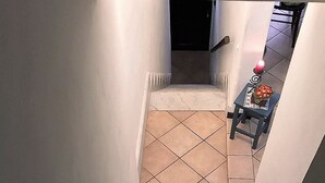 A staircase leading to a room with a tiled floor and a small table with a vase of flowers. - House Cornelia (Pietra Ligure)