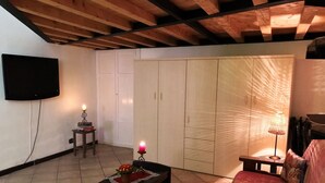 A cozy living room with a wooden ceiling, a flat-screen TV mounted on the wall, a sofa, a coffee table with a candle, and a small table with a lamp. - House Cornelia (Pietra Ligure)