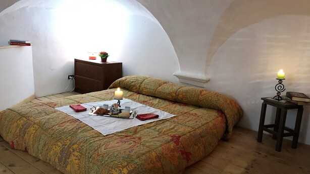 A cozy bedroom with a bed, a bedside table with a candle, and a small table with books. - House Cornelia (Pietra Ligure)