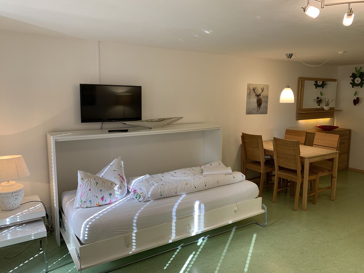 Camera da letto con un letto, comodino, lampada, televisore e zona pranzo con sedie e tavolo.