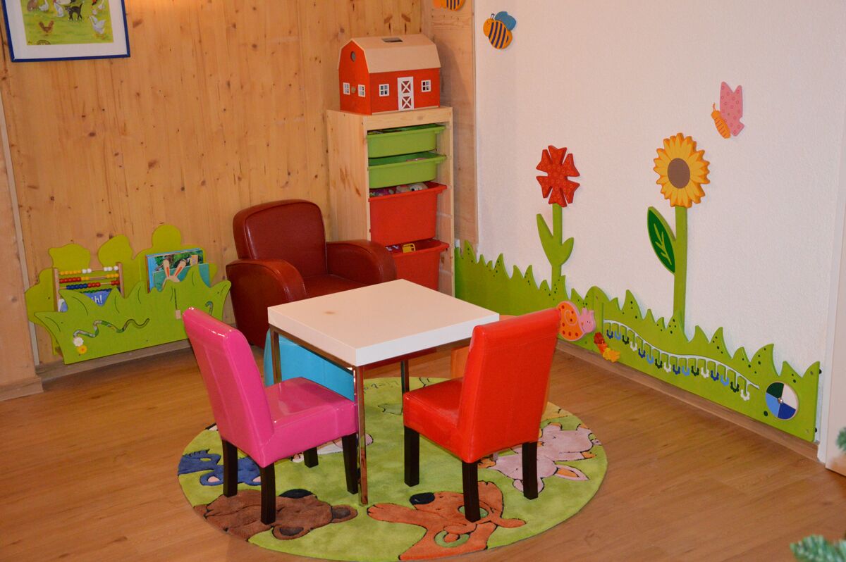 A children's playroom with a table, chairs, and a bookshelf.