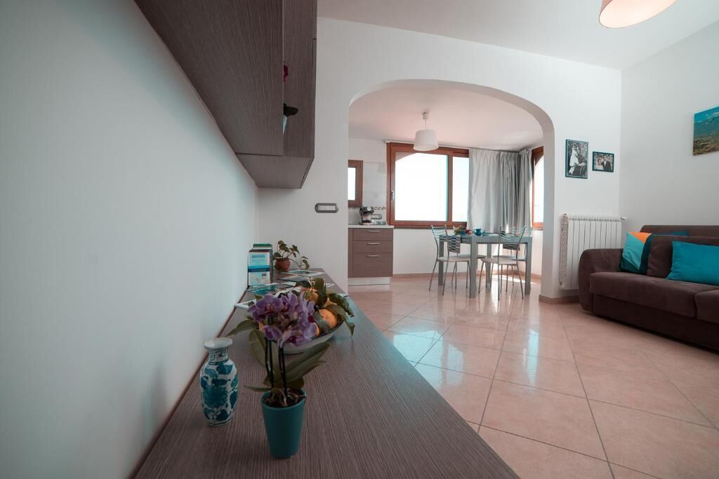 Un soggiorno moderno con un divano marrone, una zona pranzo con tavolo e sedie, e una cucina sullo sfondo.