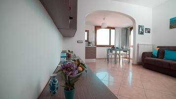 Un soggiorno moderno con un divano marrone, una zona pranzo con tavolo e sedie, e una cucina sullo sfondo.