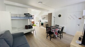 Ein kompakter Wohnbereich mit Etagenbett, einer Couch, einem Esstisch mit Stühlen und einer Küchenzeile im Hintergrund.