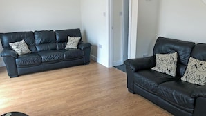A living room with two black leather sofas, each with patterned cushions, and a wooden floor. - Great property for exploring the Forest of Dean and surrounding areas. (Mile End, near Coleford)